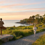 Un homme faisant du yoga sur un rocher et une femme courant sur un sentier côtier au coucher du soleil.